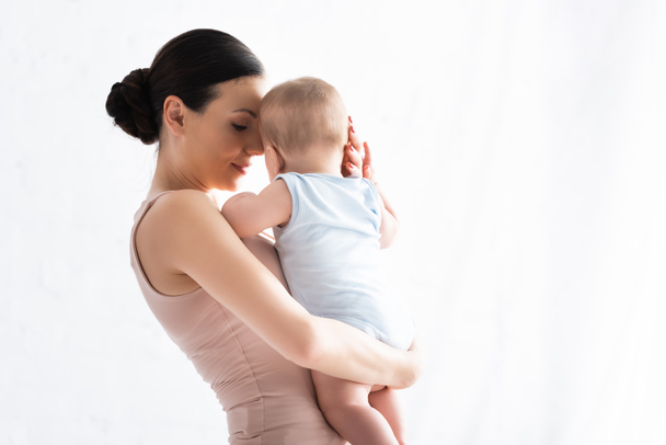 Mutter hält entzückenden Säugling im Babystrampler in den Armen  - Foto, Bild