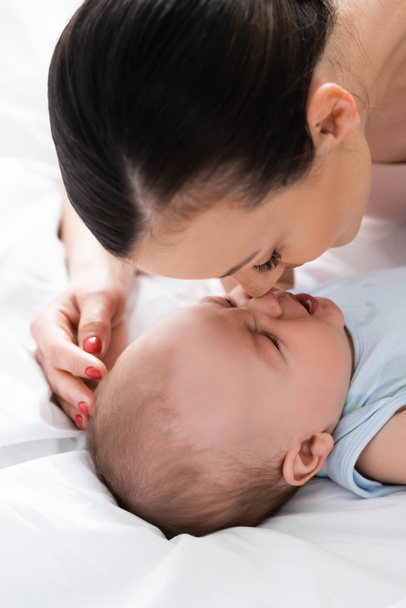 attractive mother and infant son touching noses in bedroom - Foto, immagini