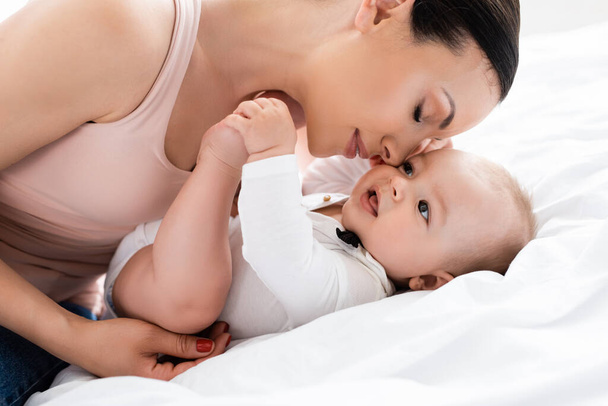atractiva madre con los ojos cerrados cerca lindo bebé hijo en la cama
 - Foto, Imagen