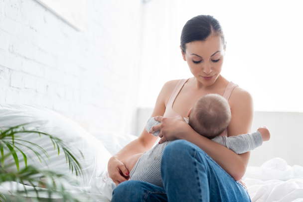 selective focus of attractive mother looking at infant son while breastfeeding in bedroom - Φωτογραφία, εικόνα