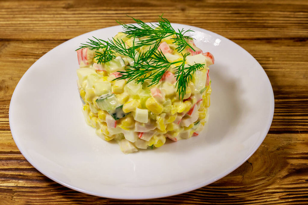 Saláta rákkal, csemegekukoricával, uborkával, tojással és majonézzel fából készült asztalon - Fotó, kép