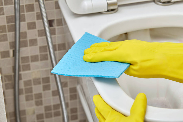 Wash the rim of the toilet with a blue cleaning cloth. Daily routine. - Photo, image