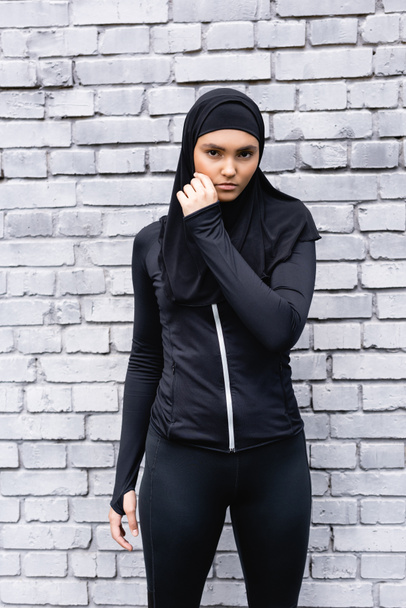junge muslimische Sportlerin im Hijab steht nahe Ziegelmauer  - Foto, Bild