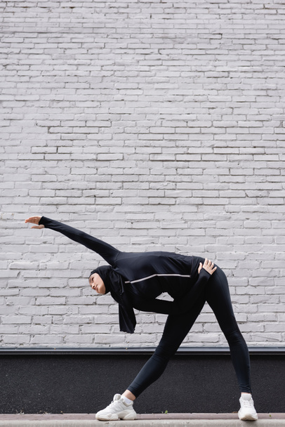 arabian sportswoman in hijab exercising near brick wall  - Fotografie, Obrázek