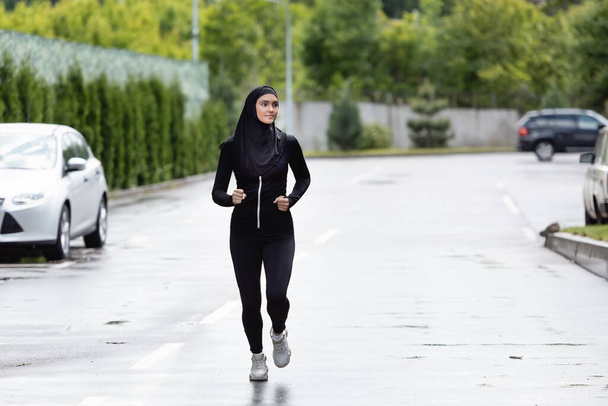 Arabe sportive dans le hijab et le jogging de vêtements de sport à l'extérieur - Photo, image