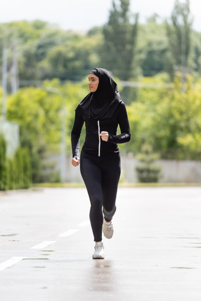 junge muslimische Sportlerin im Hijab und Sportbekleidung beim Joggen draußen - Foto, Bild
