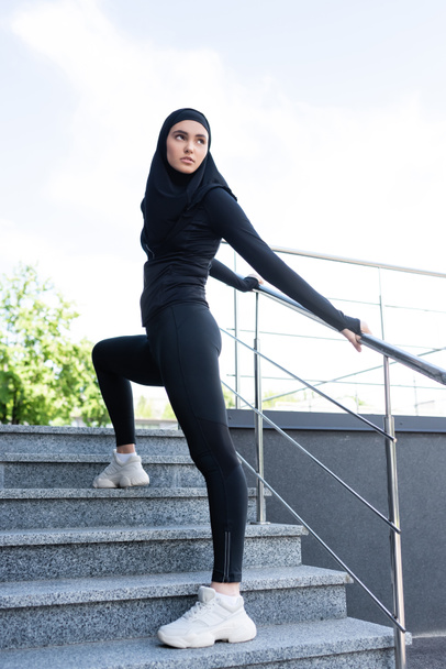 young muslim sportswoman in hijab standing on stairs outside  - Foto, Bild