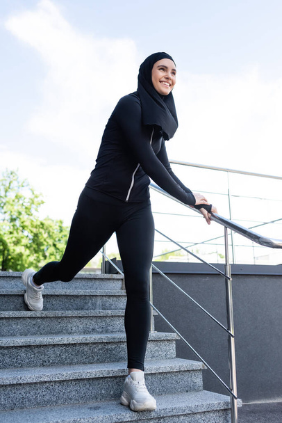 happy muslim sportswoman in hijab walking on stairs outside  - Photo, Image