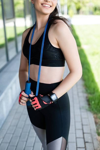 cropped view of happy woman in sport gloves holding skipping rope  - Foto, imagen
