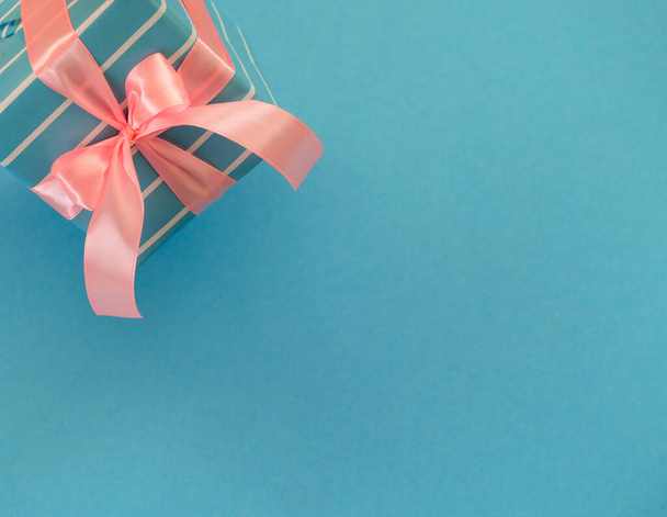 Κουτί δώρου με ροζ κορδέλα και φιόγκο σε μπλε επιφάνεια - Φωτογραφία, εικόνα