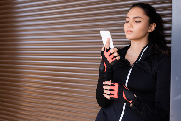 young sportswoman looking at smartphone while standing outside - Photo, Image
