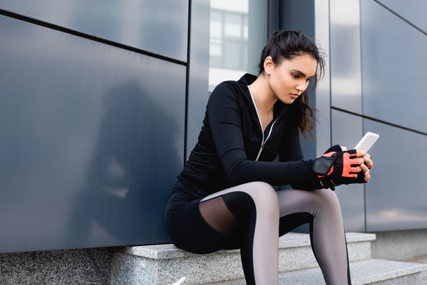 young sportswoman sitting and using smartphone outside  - Foto, Bild