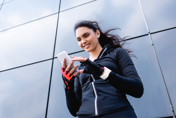 low angle view of happy sportswoman looking at smartphone  - Фото, изображение