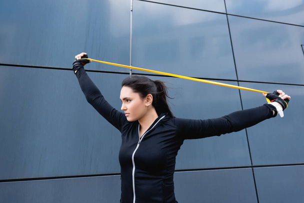 young sportswoman exercising with resistance band near building  - Foto, Imagem