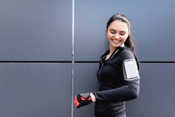 cheerful sportswoman looking at phone armband on hand  - Foto, Imagem