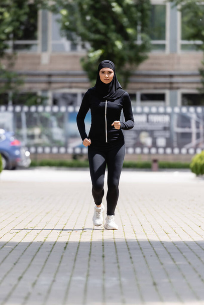 young arabian sportswoman in hijab and sportswear jogging on street  - Fotó, kép