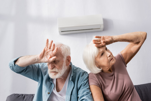 Starší pár trpí horkem, zatímco sedí pod klimatizací doma  - Fotografie, Obrázek