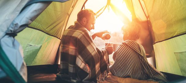 Father and son drink hot tea sitting together in camping tent - 写真・画像