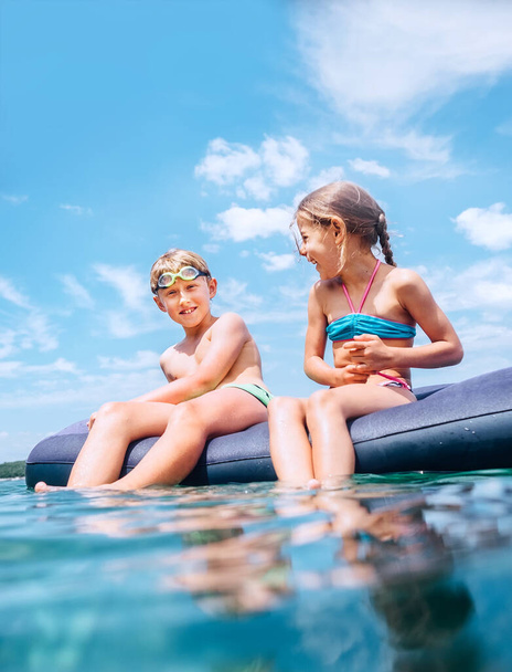 Sister and brother sitting on  inflatable mattress and enjoying the sea water, have fun when swim in the sea. Careless childhood time image. - Foto, immagini