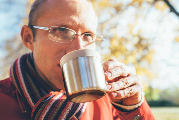 Man in Eyeglasses with cup of hot drink warming on open autumn air in the park - Foto, immagini