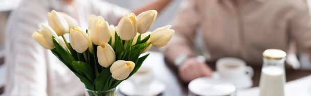 Cultura panorâmica de tulipas em vaso e casal sênior bebendo café no fundo
 - Foto, Imagem