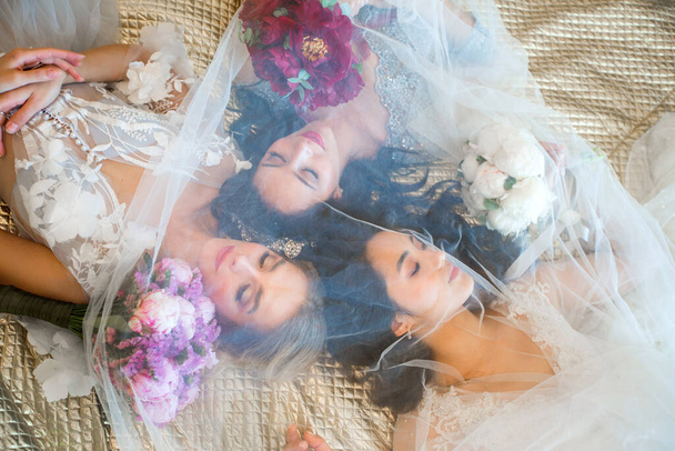 three beautiful women in dresses with bouquets of flowers lying on a sofa - Foto, Bild