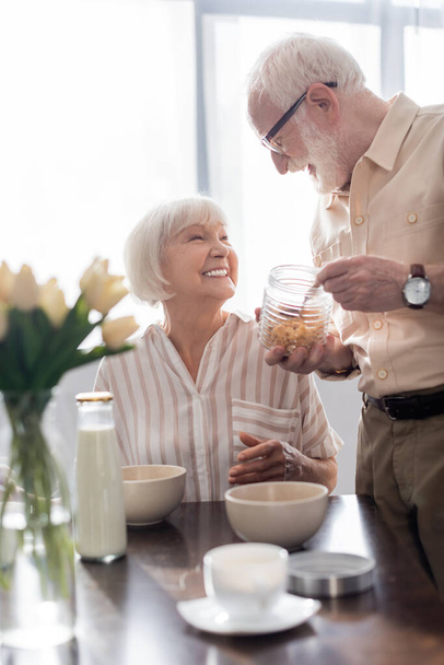 Szelektív fókusz idősek mosolyognak egymásra reggeli közben a konyhában - Fotó, kép