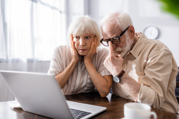 Selektiver Fokus besorgter Seniorin auf Laptop neben Ehemann zu Hause  - Foto, Bild
