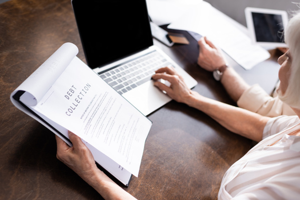 Foco seletivo da mulher usando laptop e segurando papéis com cobrança de dívidas lettering perto do homem na mesa
  - Foto, Imagem