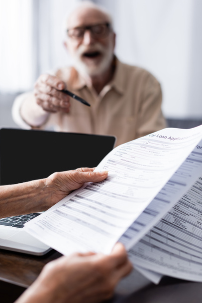 Selective focus of woman holding documents near laptop and husband pointing with pen at home  - Photo, Image