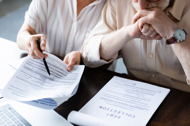 Vista recortada de la mujer mayor señalando papeles cerca de marido y documento con letras de cobro de deudas en la mesa
   - Foto, imagen