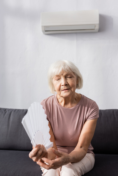Selective focus of elderly woman holding fan on couch at home  - Foto, afbeelding