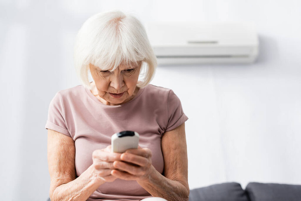 Focus selettivo della donna anziana con telecomando del condizionatore d'aria a casa  - Foto, immagini