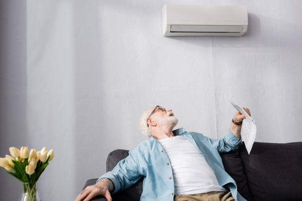 Concentration sélective d'un homme âgé tenant un journal et regardant le climatiseur à la maison  - Photo, image