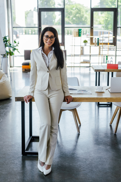 happy woman in glasses standing near table in office  - Foto, Bild