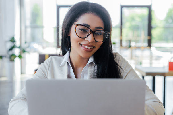 selective focus of cheerful businesswoman in glasses using laptop  - Foto, Imagen