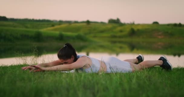 Γυναίκα τεντώνει την πλάτη της και κάνει στροφές ξαπλωμένη στο γρασίδι, κορίτσι προπονείται στο πάρκο της πόλης στη φύση. - Πλάνα, βίντεο