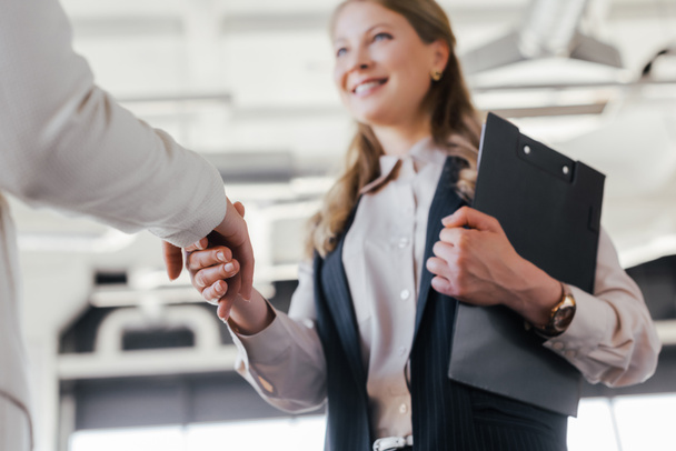 selective focus of smiling businesswoman shaking hands with coworker in office - Photo, Image