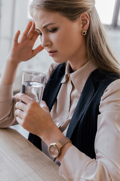 tired businesswoman having headache and holding glass of water - Photo, image