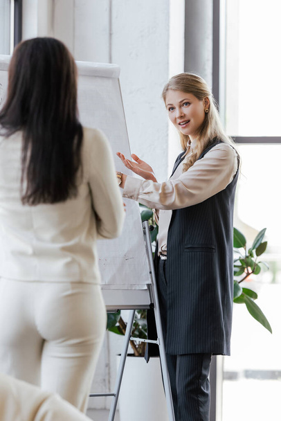 selective focus of businesswoman pointing with hand at flipchart and looking at coworker  - Photo, Image