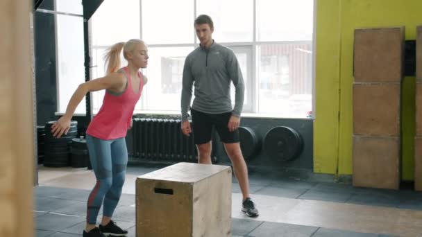 Girl in sports clothing jumping on box training while crossfit coach watching - Materiaali, video
