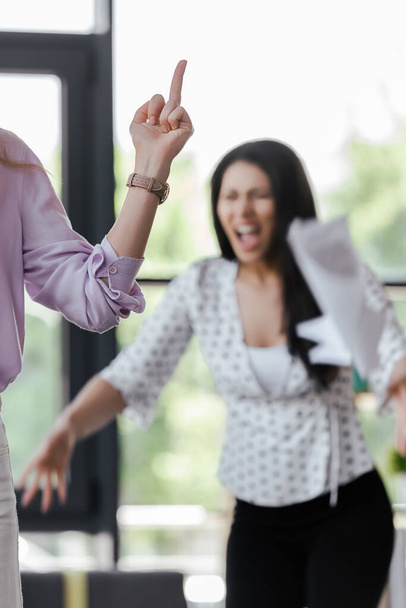 Selektiver Fokus der Geschäftsfrau zeigt wütenden Mitarbeitern den Mittelfinger  - Foto, Bild