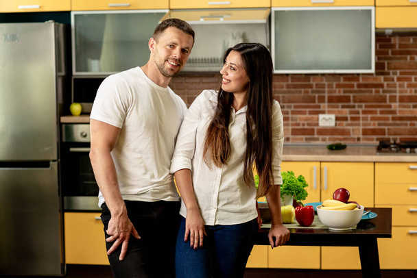 Glückliches Paar in der Küche. Mann und Frau lächeln. Frau schaut Mann an. Hinter dem Tisch Obst und Gemüse. Gesunde Ernährung - Foto, Bild