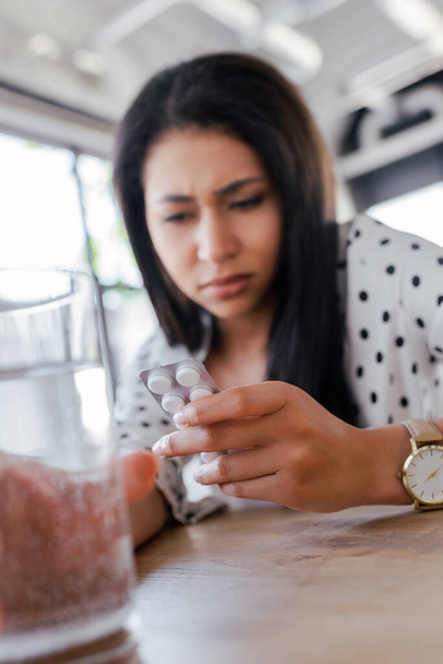 selective focus of woman holding glass of water and looking at blister pack with pills  - Valokuva, kuva