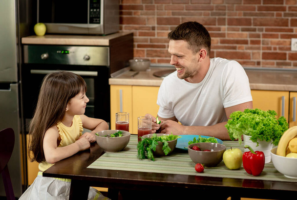 Веселый отец и его дочь завтракают вместе на кухне, разговаривают, веселятся. Здоровое питание, семейные отношения
 - Фото, изображение