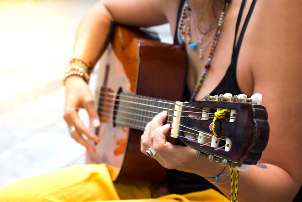 Primo piano di bella mano donna hippie con bracciali in pietra multicolore che suonano la chitarra sulla piazza all'aperto. Luce del sole sulla foto. Musica e stile di vita libero - Foto, immagini