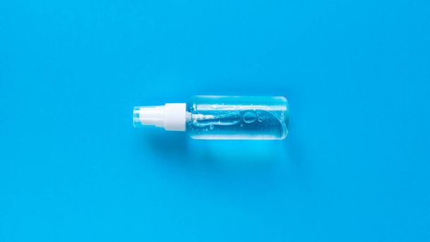 Hand sanitizer transparent bottle with spray cap at the middle of blue background. Simple flat lay with pastel paper texture. Medical concept. Stock photography. - Fotó, kép