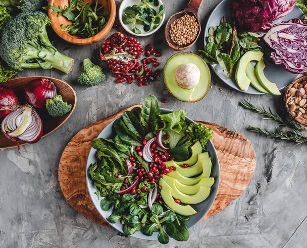 Gezonde verse salade met avocado, groenten, arugula, spinazie, granaatappel op schaal over grijze achtergrond. Gezond veganistisch eten, schoon eten, dieet, bovenaanzicht - Foto, afbeelding