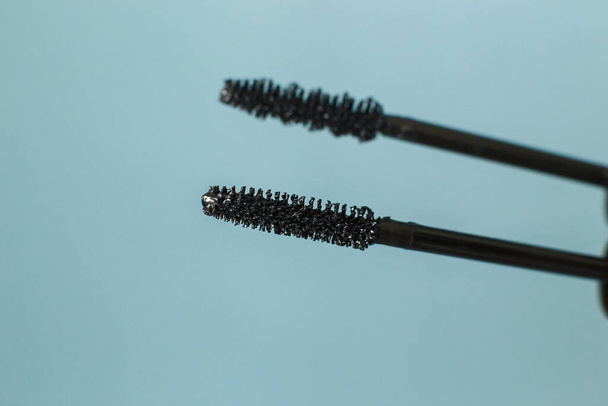 Woman holding mascara makeup brushes on the soft blue copyspace background - 写真・画像