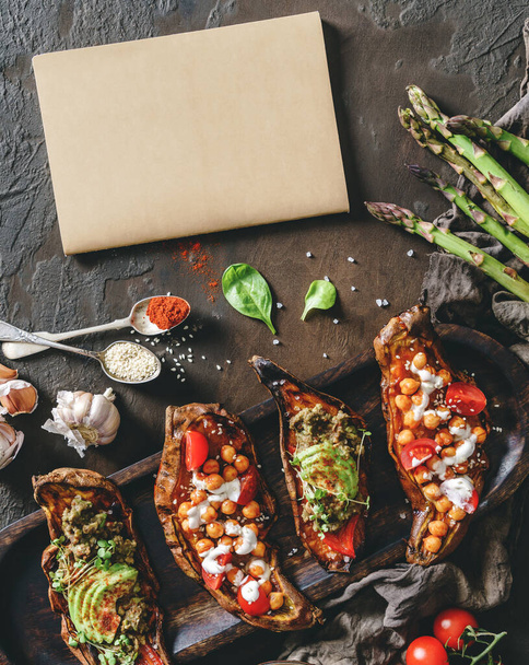 Baked sweet potato toasts with roasted chickpeas, tomatoes, goat cheese, avocado, seedlings on wooden board over brown background, empty notepad. Healthy vegan food, clean eating, toning - Photo, Image